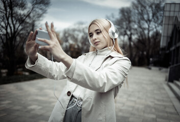 Young stylish girl with headphones makes selfie outdoors