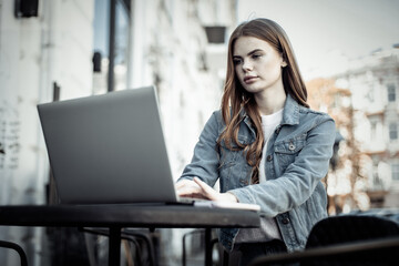 Young beautiful woman freelancer using laptop while sitting at table in outdoor cafe