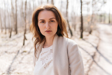 Beautiful girl in a white dress and a beige coat in a spring birch grove. High quality photo