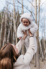 A beautiful young mother in a white dress and a beige coat with a baby in a spring birch grove. High quality photo