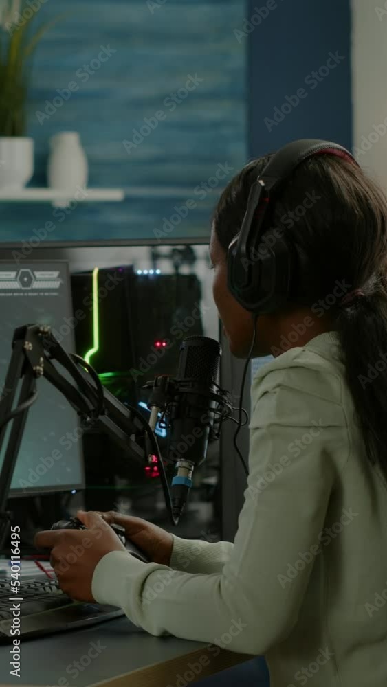 Poster vertical video: black woman streamer playing videogames with joystick talking with teammates on stre