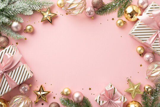 Christmas concept. Top view photo of present boxes fir branches in snow decorated with stylish baubles star ornaments and confetti on isolated light pink background with blank space in the middle