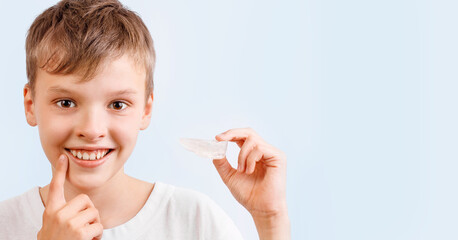 Positive child boy is holding mouth guards for his teeth and smiling. Banner. Invisible braces helps of orthodontics problem. Close-up portrait. Mobile appliance for dental teeth correction. - obrazy, fototapety, plakaty