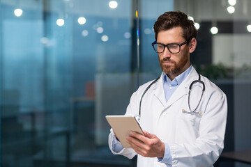 A serious and thoughtful doctor reads medical information from a tablet computer, a man in a...
