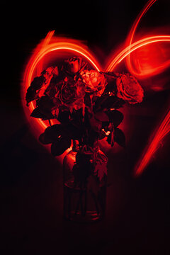 Red neon rose with heart shape lights background. Abstract red dark rose bouquet, neon light, glare. Magic flower.