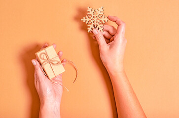 Gift box and wooden snowflake in female hands on a beige background.