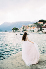 Fototapeta na wymiar Bride holds the hem of her dress in her hand on the banks of Perast