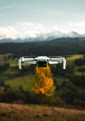 Close up photo of small white drone flying in the air with beautiful scenic view of the green meadows and snowy mountains on background. Vertical detailed photo of drone (uav) in colorful scenery.