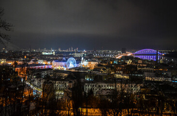 Fototapeta premium Aerial evening view to Kontraktova Square with Christmas market, New Year tree and ferris wheel during celebration. Kyiv, Ukraine