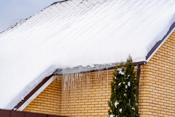 Icicles on roof of private house resulting from improper construction of roof. Metal Downpipe...
