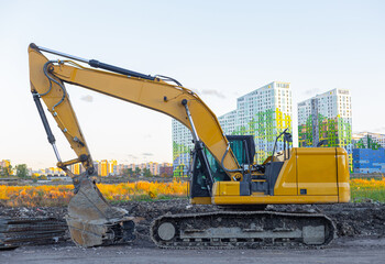 The tracked orange backhoe loader is parked with the bucket lowered. The crawler excavator is parked on the street.