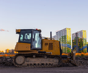 Parked, yellow crawler bulldozer side view against the backdrop of the urban landscape.