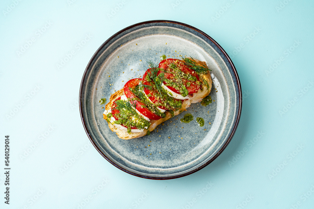 Wall mural bruschetta with tomato mozzarella and pesto on a plate on a colored background