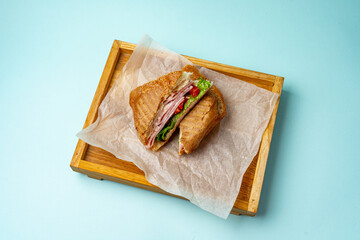 sandwich with ham greens and tomato on a wooden board on a colored background
