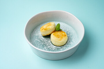 syrniki with powder in a plate on a colored background