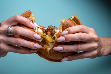 hands tear open burger on turquoise background
