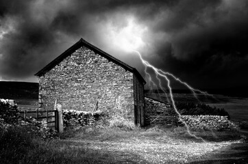 Black and white shot of bright lightning strike in dark sky near old abandoned house in countryside