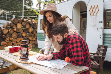Young beautiful loving couple travelling across country in the van. Millennial man and woman in a travel camper. Cozy atmosphere, vacations vibe. Drinking tea, choosing new destination on a map