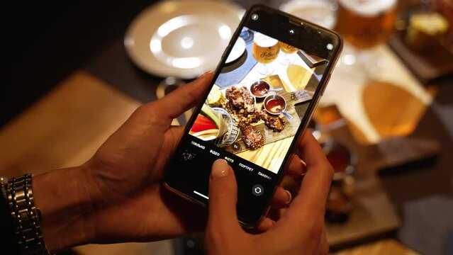 A girl takes a photo of a dish she ordered in a restaurant on her phone
