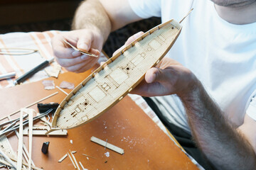 Hands of man adjusts plywood details for ship model, grinding on sandpaper. Process of building toy...