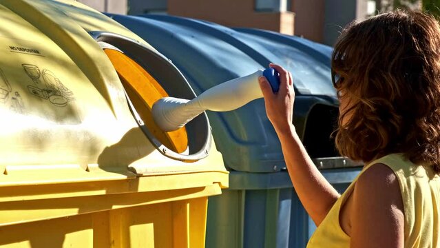woman with curly brown hair and yellow dress throwing a white plastic container into the recycling bin