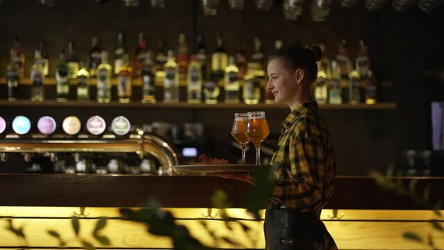 Attractive young girl waiter carries glasses with beer on a tray
