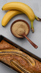 fresh banana bread surrounded by fresh bananas and cooking ingredients lies on a plain gray background close-up. fresh pastries, organic food, vegetarian food
