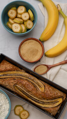 fresh banana bread surrounded by fresh bananas and cooking ingredients lies on a plain gray background close-up. fresh pastries, organic food, vegetarian food