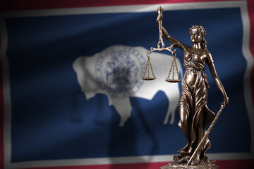 Wyoming US state flag with statue of lady justice and judicial scales in dark room. Concept of...