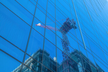 Skyscraper with glass that reflects a construction crane and unfinished building