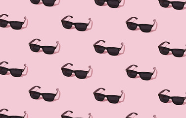 A pattern of black sunglasses on a light pink background. Summer accessories and fashion detail on vacation. Art minimal creative concept.