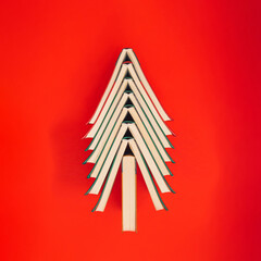 Colorful books arranged in the shape of a Christmas tree on vibrant red background. Creative...