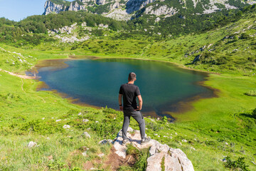 A man standing on the rock and watching blue lake surrounded with with amazing nature.
