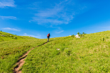 A man walks on a path and heading to the peak of mountain, under the blue sky.