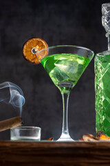 green liquor drink in cocktail glass with lemon slice and cigar smoking on light bar