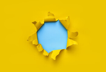 Torn hole in yellow paper with blue empty background. Copy space, mockup. Place for text or logo.