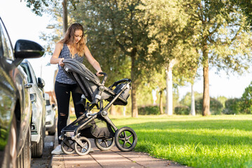 Mother preparing the baby stroller in the park after parking the car