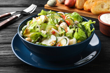 Bowl of delicious cucumber salad served on black wooden table, closeup