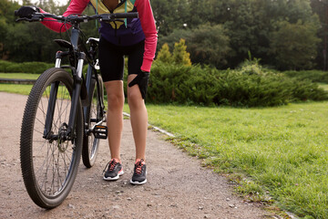 Naklejka premium Woman with injured knee and bicycle outdoors, closeup. Space for text