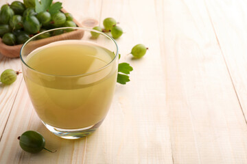 Tasty gooseberry juice in glass on wooden table. Space for text