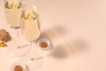 Glasses of delicious sparkling wine and chocolate truffles on pale pink background. Space for text