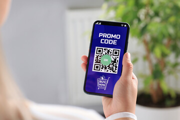 Woman holding smartphone with activated promo code in online shopping app indoors, closeup