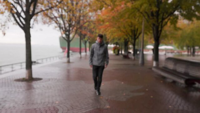Young Caucasian male with attitude walks towards camera, pulls up hood in the rain downtown Toronto
