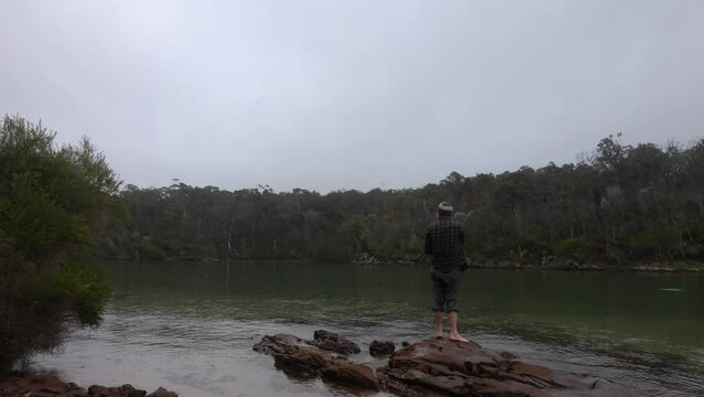 A man casts a fishing line into a calm bay on the far south coast of NSW Australia.