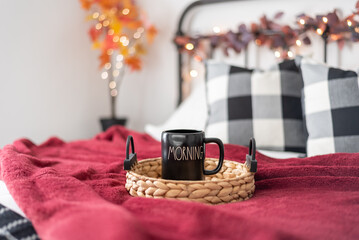 Coffee mug on a tray on a cozy bed styled for fall