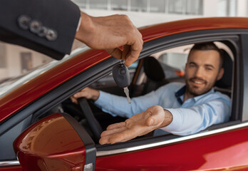  Young man sitting inside new car and getting keys to it. Concept for car rental