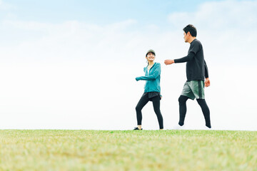 青空の見える公園を健康のためウォーキングしてダイエットしている男女
