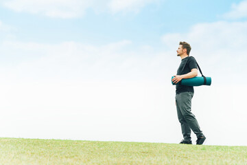 公園でヨガマットを持って歩くスポーツウェアの白人男性（パークヨガ）

