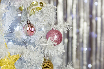A variety of pink and gold decorations on a white Christmas tree.