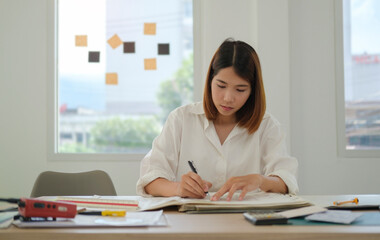 Young asian female architect sitting at desk in office and working over building designs